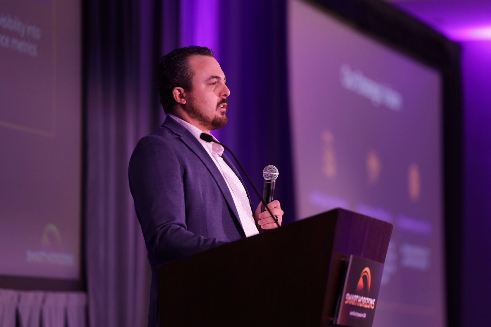 Speaker presenting at a podium in front of a purple-lit screen